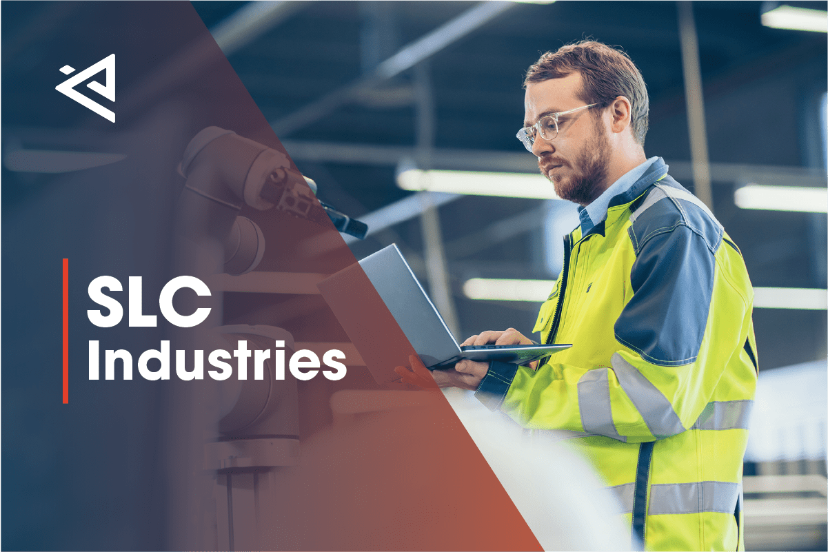 man with brown hair, safety goggles, and a reflective jacket fixing a robotic arm with a laptop