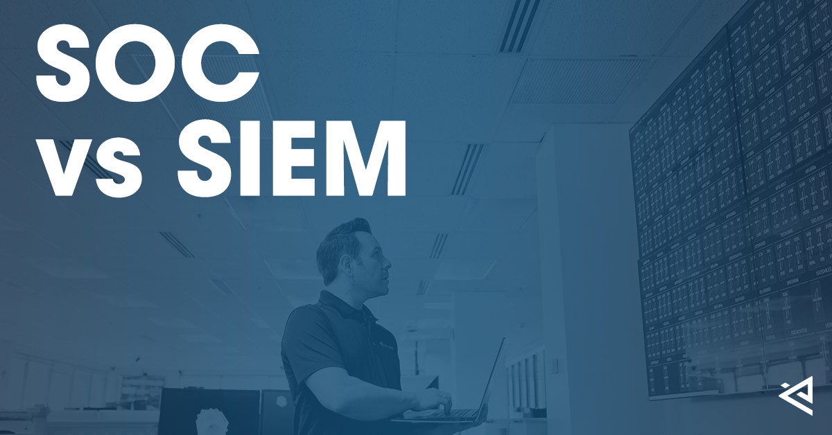 Man holding a laptop staring at tech stats on a large monitor